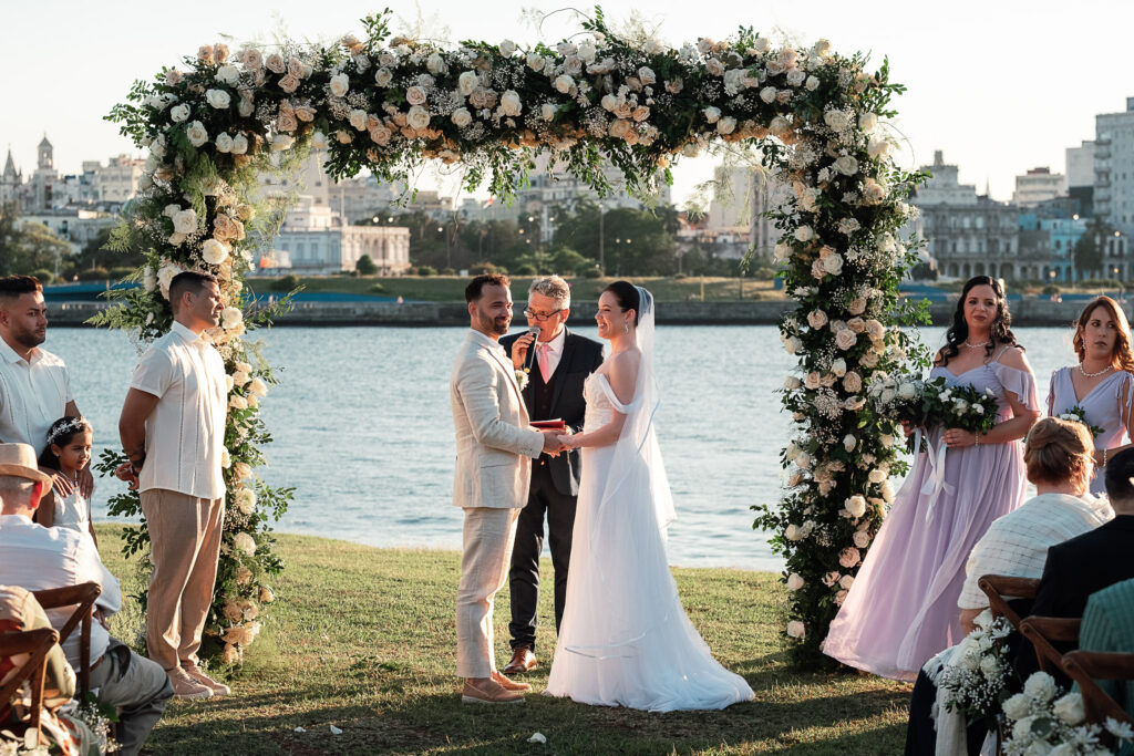 Los novios se toman de la mano en el gazebo con vista al mar y La Habana, rodeados de invitados