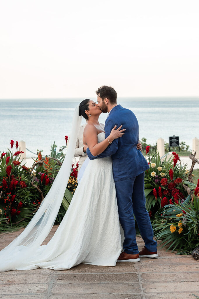 Couple kissing during the ceremony with warm flowers and the sea in the background at the Hotel Nacional