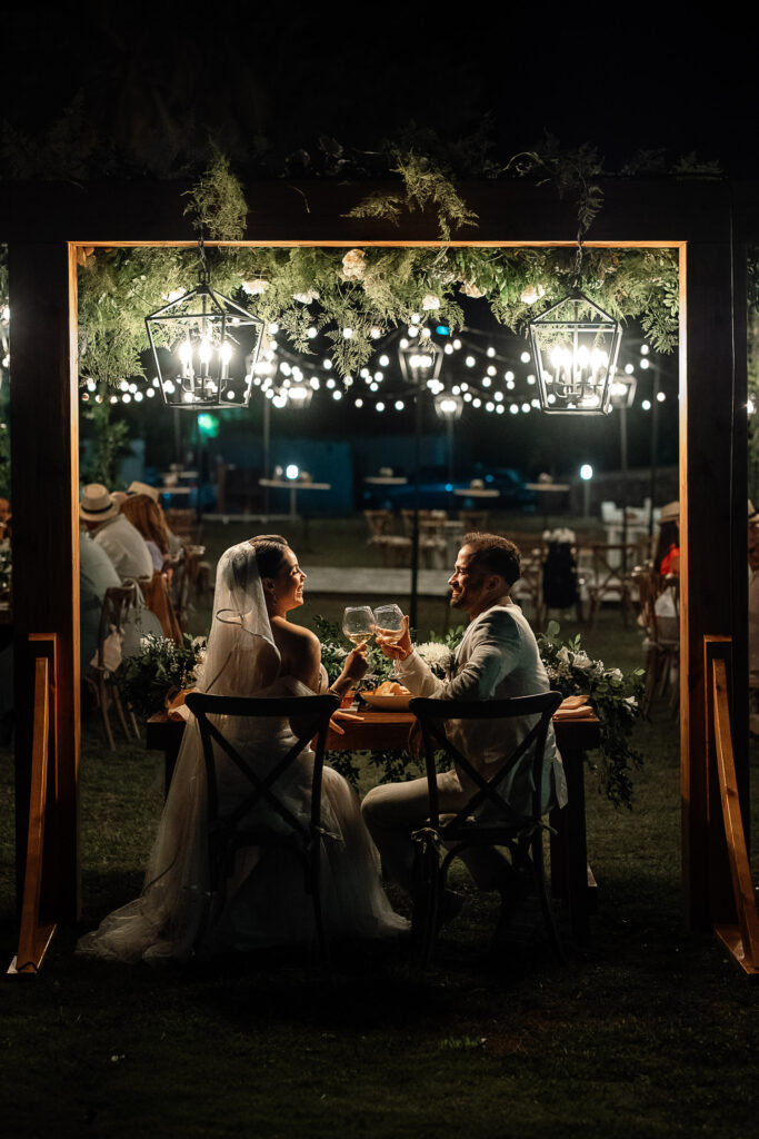 Novios brindan sentados en la mesa presidencial decorada con flores blancas