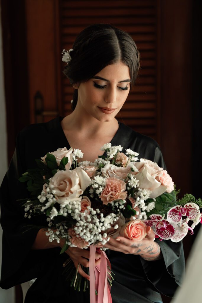 Bride in a black robe looking at her bouquet during the wedding preparations in Havana