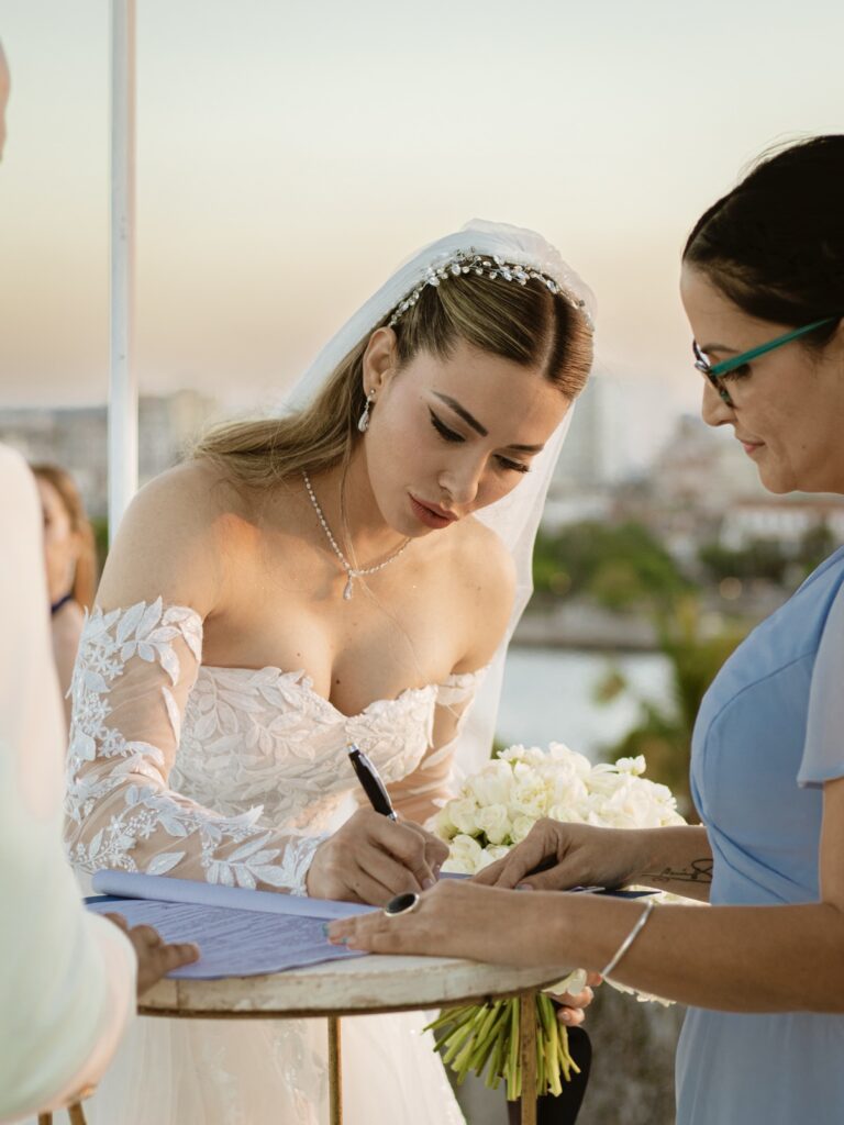 Bride signing the legal marriage certificate during a civil and religious combined wedding ceremony at El Morro, Cuba.