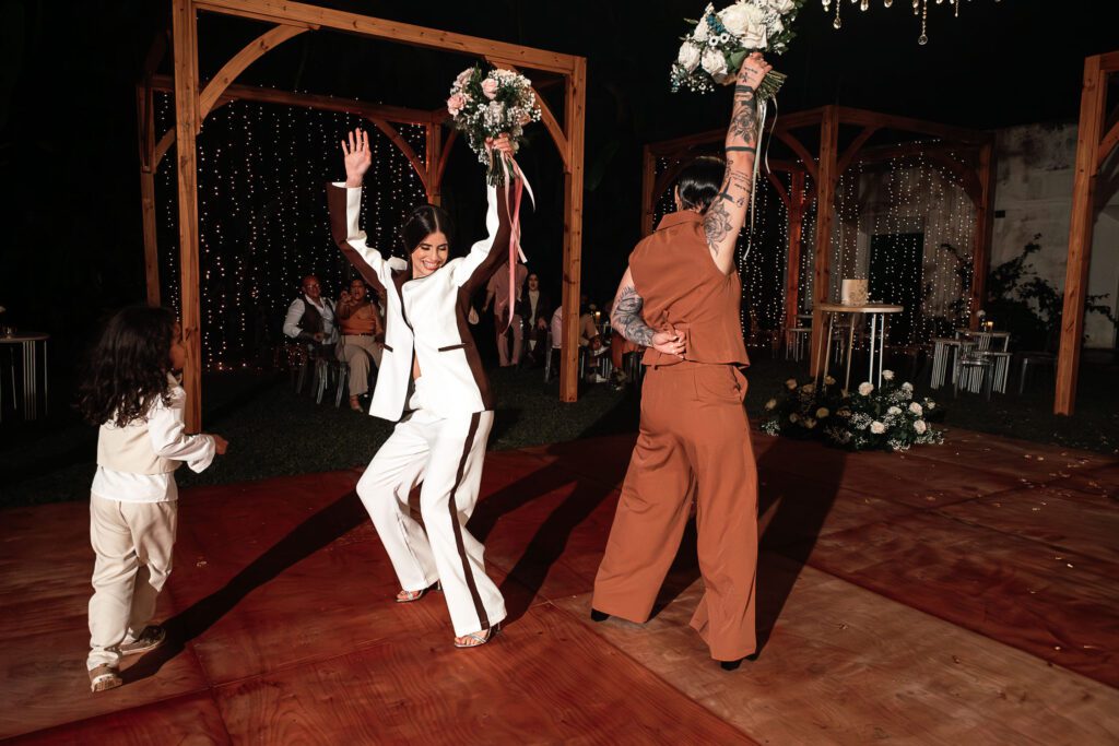 The two brides raise their bouquets while dancing on the floor at their wedding in Cuba under the most beautiful dome