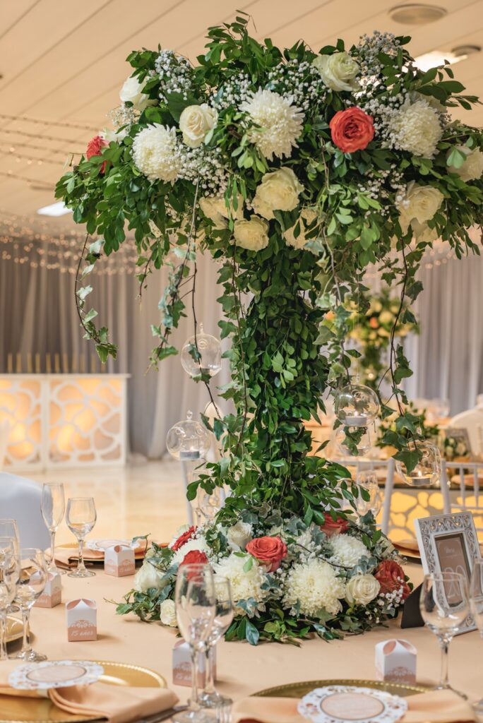 Centro de mesa elevado con rosas, crisantemos y follaje en salón de fiesta de quince