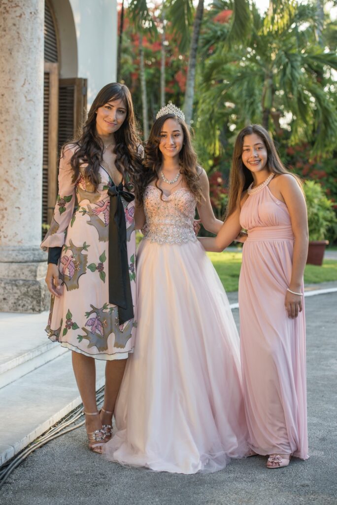 La quinceañera posa sonriente con familiares en el jardín, vestida con un vestido rosa pálido y tiara