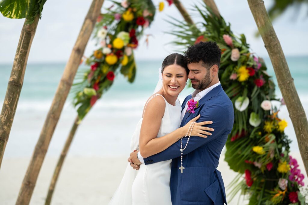 novios-abrazados-durante-boda-en-la-playa-de-varadero-con-arco-floral-tropical